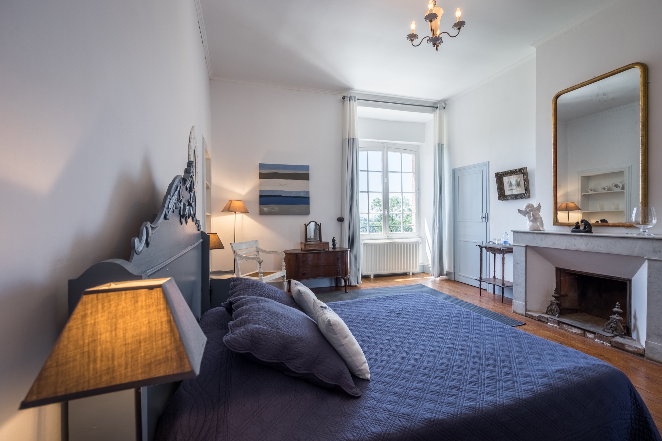 Vue principale de la Chambre du Pastel avec lit bleu, cheminée en marbre et fenêtre sur le parc