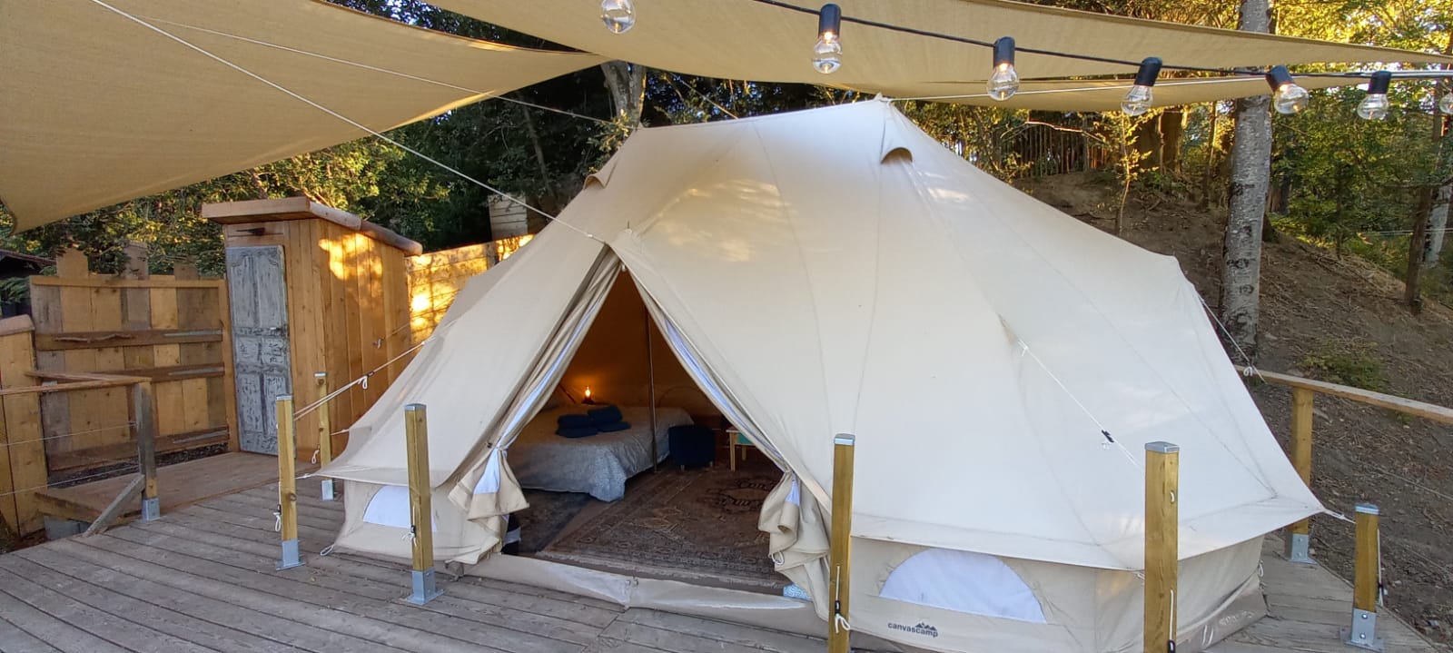 Vue extérieure du lodge Belle de nuit avec terrasse boisée et entrée sous toile
