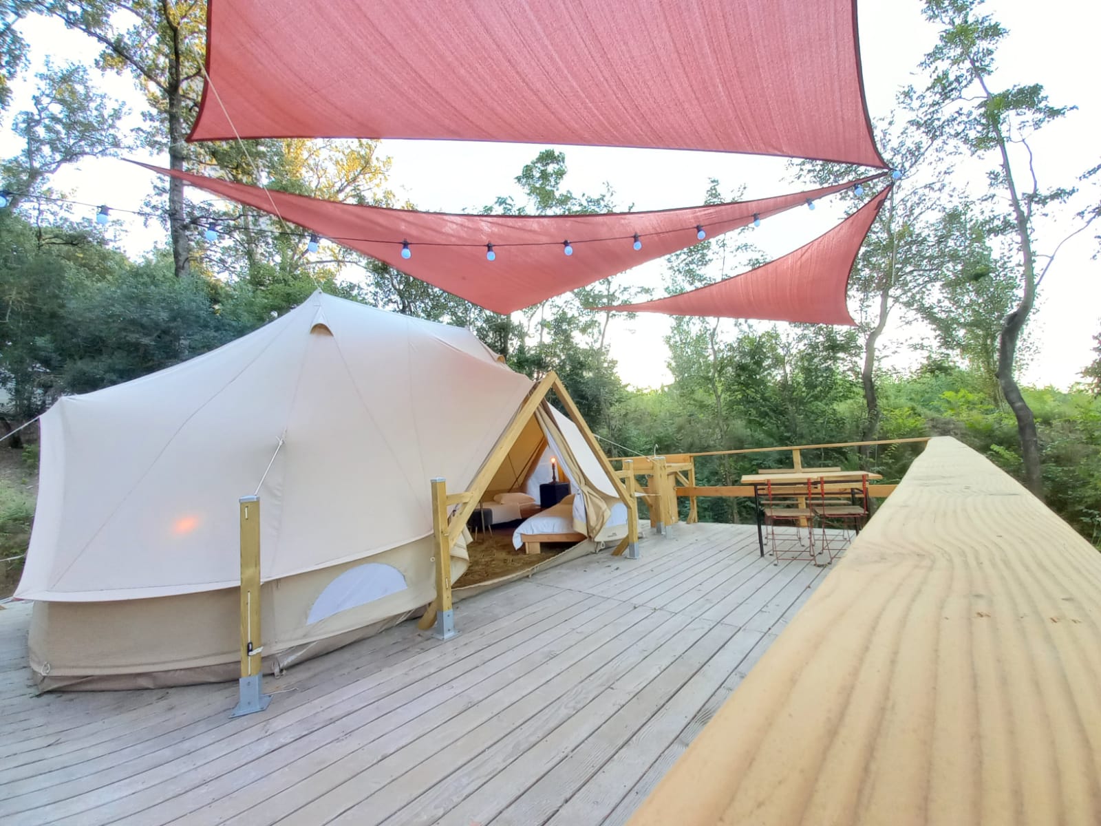 Vue extérieure du lodge Chèvrefeuille avec terrasse boisée et voiles d’ombrage rouges